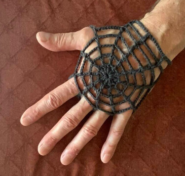 Fingerlose gehäkelte Handstulpe mit Spinnennetz-Muster in Dunkelgrau auf einer Hand