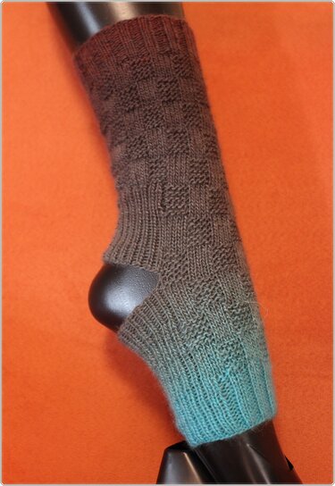 Gestrickte Damen‑Beinstulpen Braun‑Türkis Farbverlauf mit Fersenöffnung und Strukturmuster, präsentiert auf schwarzem Beinmodell vor orangefarbenem Hintergrund.