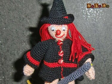 Handgehäkelte Hexenfigur mit rotem Haar, schwarzem Spitzhut, roter Nase und großen Augen, die einen kleinen Besen hält