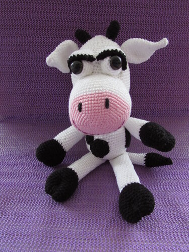 Gehäkelte Amigurumi Kuh in Weiß und Schwarz mit rosa Schnauze auf violettem Hintergrund