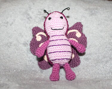 Kleiner gehäkelter Schmetterling in Rosa und Lila mit schwarzen Augen und Antennen