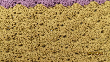 Nahaufnahme eines gehäkelten senfgelben Musters mit Büschelmaschen und lila Rand