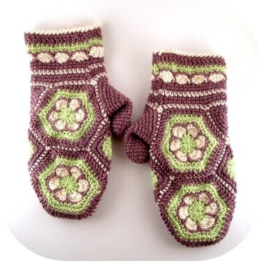 Handgehäkelte Fäustlinge in Lila, Hellgrün und Creme mit sechseckigen Blumenmotiven und texturierten Bündchen.