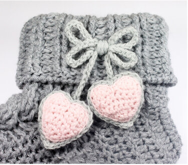 Grau gehäkelte Socke mit rosa Herzen und grauer Schleife.