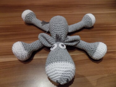 Gehäkeltes graues Amigurumi mit weißen Pfoten und langen Beinen auf Holzuntergrund