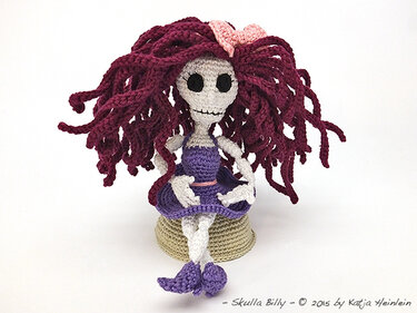 Gehäkelte Amigurumi‑Skelettpuppe mit bordeauxfarbenem Garnhaar und lila Kleid, sitzend