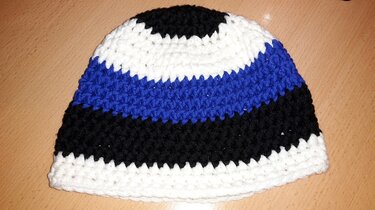 Gehäkelte, gestreifte Mütze in Weiß, Schwarz und Blau auf Holzuntergrund