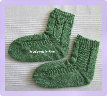 Zwei gestrickte grüne Babysocken mit geripptem Bündchen und Eulenmotiv