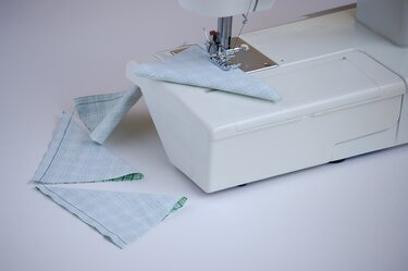 Weiße Nähmaschine näht ein hellblau-kariertes Stoffdreieck, mehrere fertige Dreiecke liegen daneben.