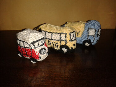 Drei gehäkelte Mini-Transporter in Rot-Weiß, Gelb-Schwarz und Blau-Gelb