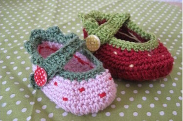 Zwei gehäkelte Babyschuhe; links rosa mit grünem Riemen und Punkten, rechts rot mit grünem Rand und Knopf