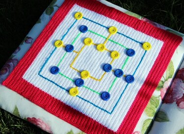 Quadratisches gehäkeltes Spielbrett weiß mit rotem Rand und aufgenähten gelben und blauen Markern