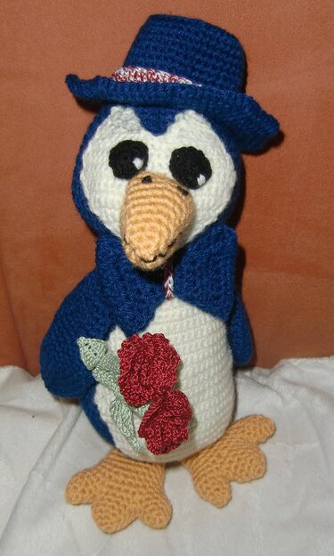 Gehäkelter blauer Amigurumi-Pinguin mit Hut, Schal und roten Rosen