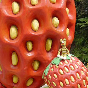 Striped knitted tiger amigurumi seated on a red strawberry sculpture.