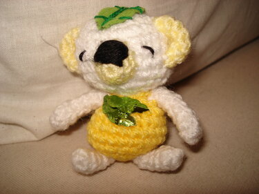 Gehäkeltes Koala-Amigurumi weiß mit gelbem Bauch und grünen Blättern, sitzend