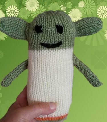 Handgehaltenes gestricktes Amigurumi mit zylindrischem weißen Körper, grünem Kopf und großen Ohren, mit orangefarbenem Rand.