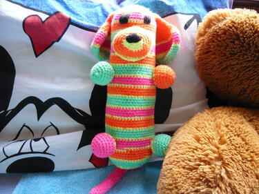 Gehäkeltes Amigurumi-Hündchen mit bunten Streifen auf einem Kissen