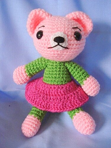 rosa Amigurumi-Bär sitzend mit sichtbarer Maschenstruktur, grünem Oberteil und pinkem Rock
