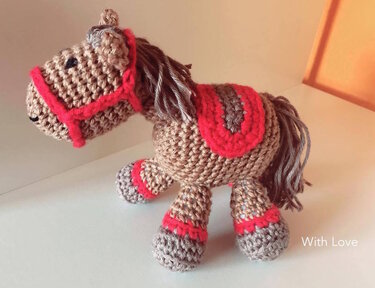 Gehäkeltes Amigurumi-Pferd in Braun mit rotem Zaumzeug und Sattel