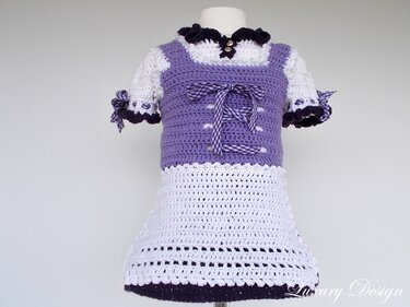 Gehäkeltes Kinderkleid im Trachtenstil in Lila und Weiß mit Schnürband auf Schaufensterpuppe