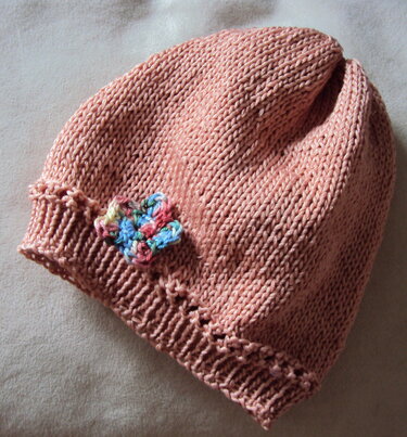 Rosafarbene gestrickte Babymütze mit Rippenbund und mehrfarbiger Häkelblume