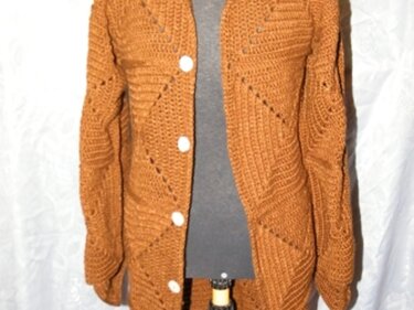 Rostbraune gehäkelte Damenjacke mit diagonalem Muster und hellen Knöpfen an einer Schaufensterpuppe