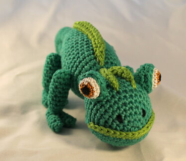 Detailaufnahme gehäkeltes grünes Amigurumi mit sichtbaren Maschen, angenähten Augen und Zierbordüre