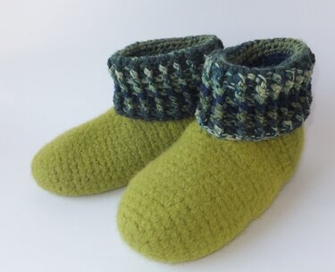 Paar lindgrüner gefilzter Hausschuhe mit umgeschlagenem, gehäkeltem Bündchen in Blau- und Grüntönen.