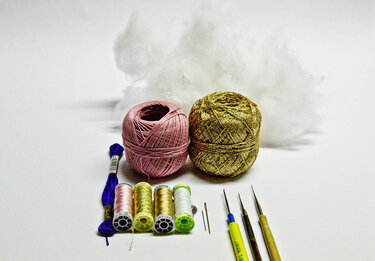 Zwei Garnknäuel (rosa und gold), mehrere Garnspulen, Stickgarn, Häkelnadeln, Nähnadeln und Füllwatte auf weißem Hintergrund