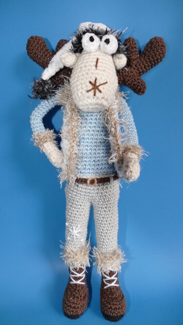 Gehäkelter Elch Amigurumi mit Mütze, hellblauem Pullover und braunen Stiefeln vor blauem Hintergrund