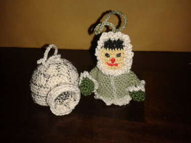 Zwei gehäkelte Schlüsselanhänger: grüne Kapuzenfigur und weißer glockenförmiger Anhänger mit Schlaufen