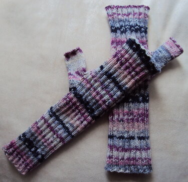 Gestrickte, fingerlose Armstulpen in Lila-, Pink-, Blau- und Cremefarben mit Rippenmuster und dunklen Querstreifen.