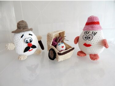 Zwei gehäkelte Amigurumi-Eier mit Hüten und ein kleiner gehäkelter Wagen mit Baby-Ei