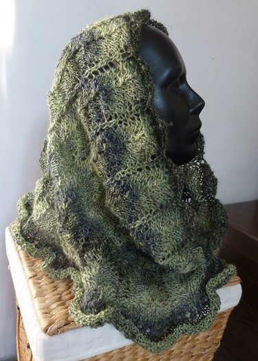 Gestrickter grüner Loop-Schal mit Ajourmuster und gewellter Kante auf schwarzem Schaufensterkopf drapiert