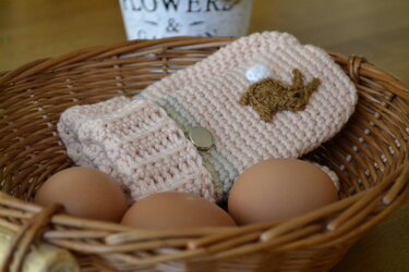 Kleiner rosafarbener gehäkelter Osterbeutel mit Hasenmotiv und Druckknopf im Weidenkorb mit Eiern