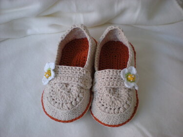 Pair of beige crocheted women's slippers with orange trim and small white flower appliqués.