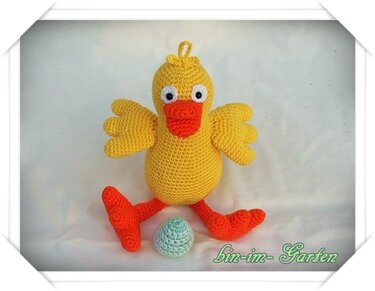 Gehäkeltes gelbes Küken-Amigurumi mit orangefarbenem Schnabel und Beinen, neben einem hellblauen Häkel-Ei