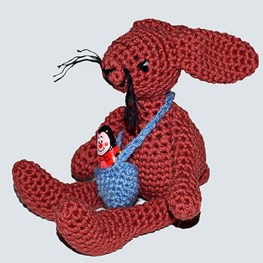 Gehäkelter rotbrauner Amigurumi-Hase sitzend mit blauer Tasche und kleiner Puppe
