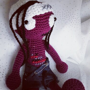 Violette Amigurumi-Häkelpuppe mit weißem Kopf, schwarzen Haarsträhnen und Jeansrock mit Sicherheitsnadel
