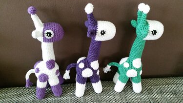 Drei gehäkelte Giraffen‑Amigurumi in Weiß, Lila und Grün mit Punkten