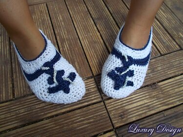 Weiße und dunkelblaue gehäkelte Ballerina-Slipper mit Anker-Applikation auf Holzplanken.
