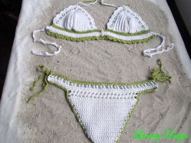 Gehäkelter weißer Bikini mit grüner Borte, liegend auf Sand