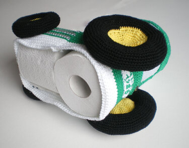 gehäkelte Toilettenpapier-Hülle in Form eines grünen Autos mit schwarzen Rädern und sichtbarer WC-Rolle