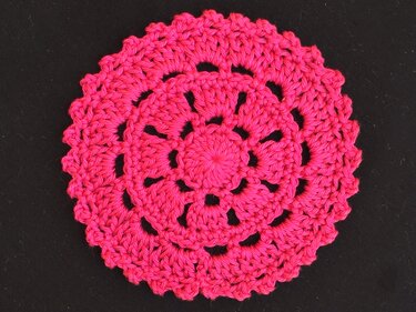 Filigraner, runder Häkeluntersetzer in kräftigem Pink vor schwarzem Hintergrund