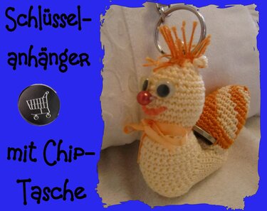 Nahaufnahme eines gehäkelten Schnecken‑Schlüsselanhängers in Creme und Orange mit Kulleraugen und Rückenschlitz für einen Einkaufschip.
