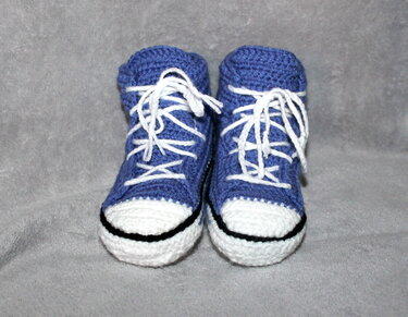 Paar gehäkelter Babysneaker blau mit weißer Zehenkappe und weißen Schnürsenkeln auf grauem Stoff
