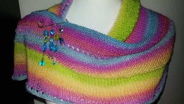 Gestricktes Tuch in Regenbogenfarben mit blauer Perlenbrosche auf einer Schneiderpuppe