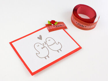 Selbstgemachte weiße Karte mit rotem Rand, zwei gezeichnete Vögel, Herz und rotes Zierband mit 'Liebe'