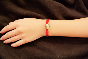 Rotes Kordelarmband mit Blumenperle am Handgelenk