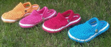Vier gehäkelte Slipper in Orange, Pink, Rot und Blau auf Gras mit weißem Sohlensaum